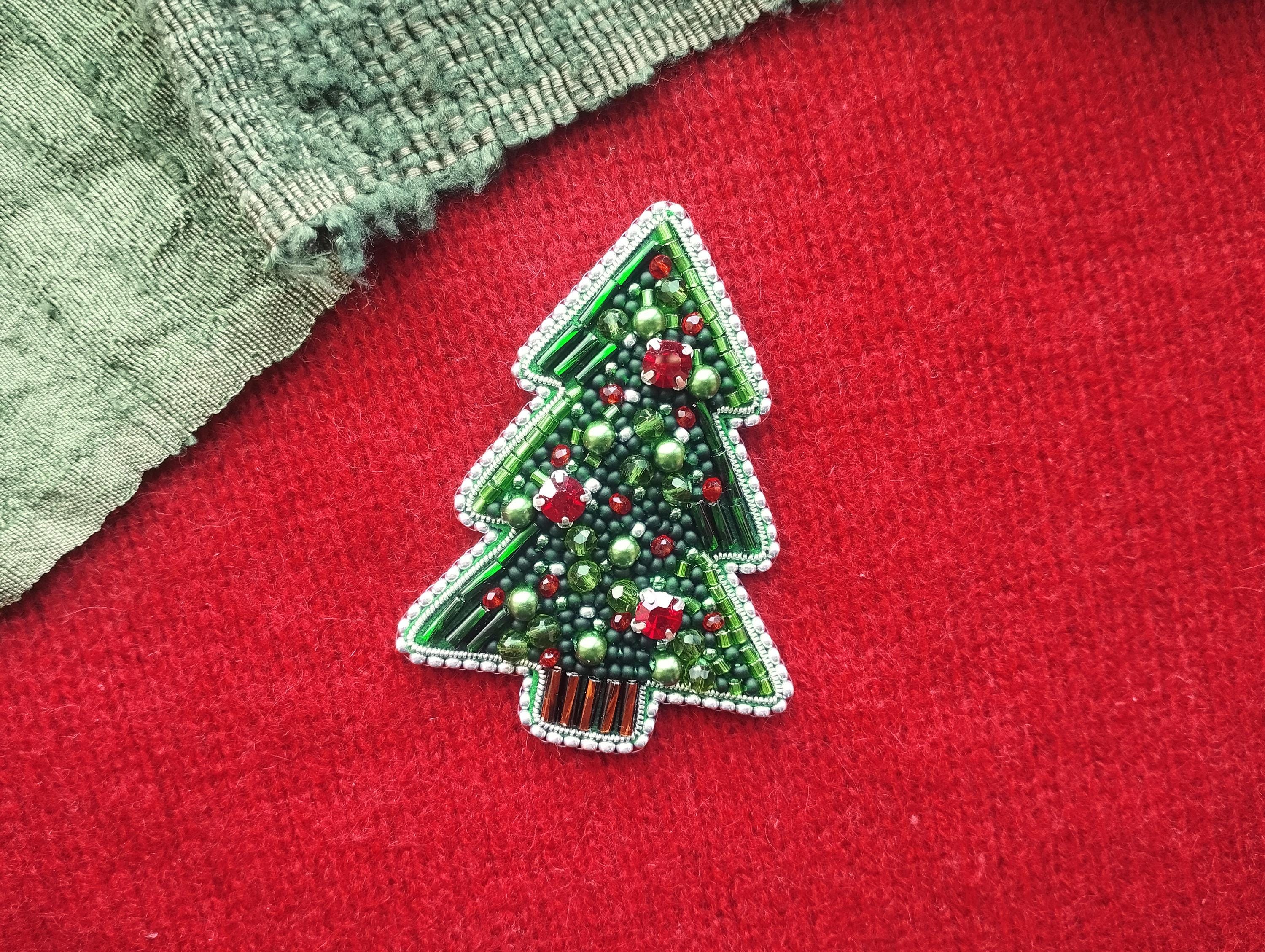 A green and red beaded Christmas tree brooch is displayed on a red fabric surface.